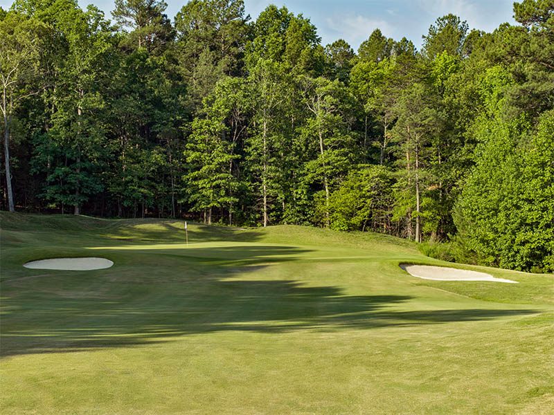Golf course green surrounded by dense trees with sand bunkers positioned on both sides.