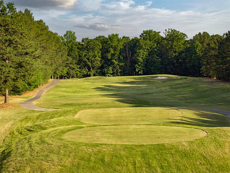 Golf course tee boxes overlooking a tree-lined fairway with a sand bunker near the green.